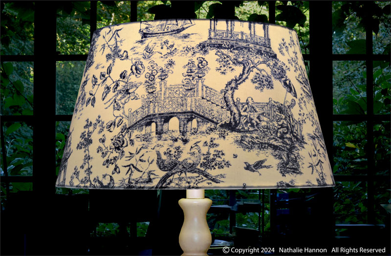 Éclairage de décoration pour luminaire de forme tambour sur pied de lampe en tissu à motif esprit toile de Jouy couleur bleu.