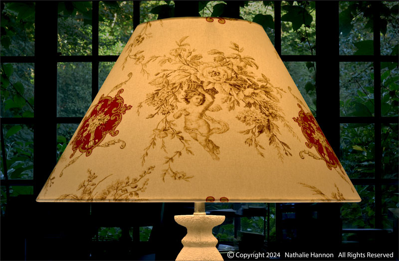 Éclairage décoratif de forme conique sur pied de lampe en tissu imprimé inspiration toile de Jouy anges.